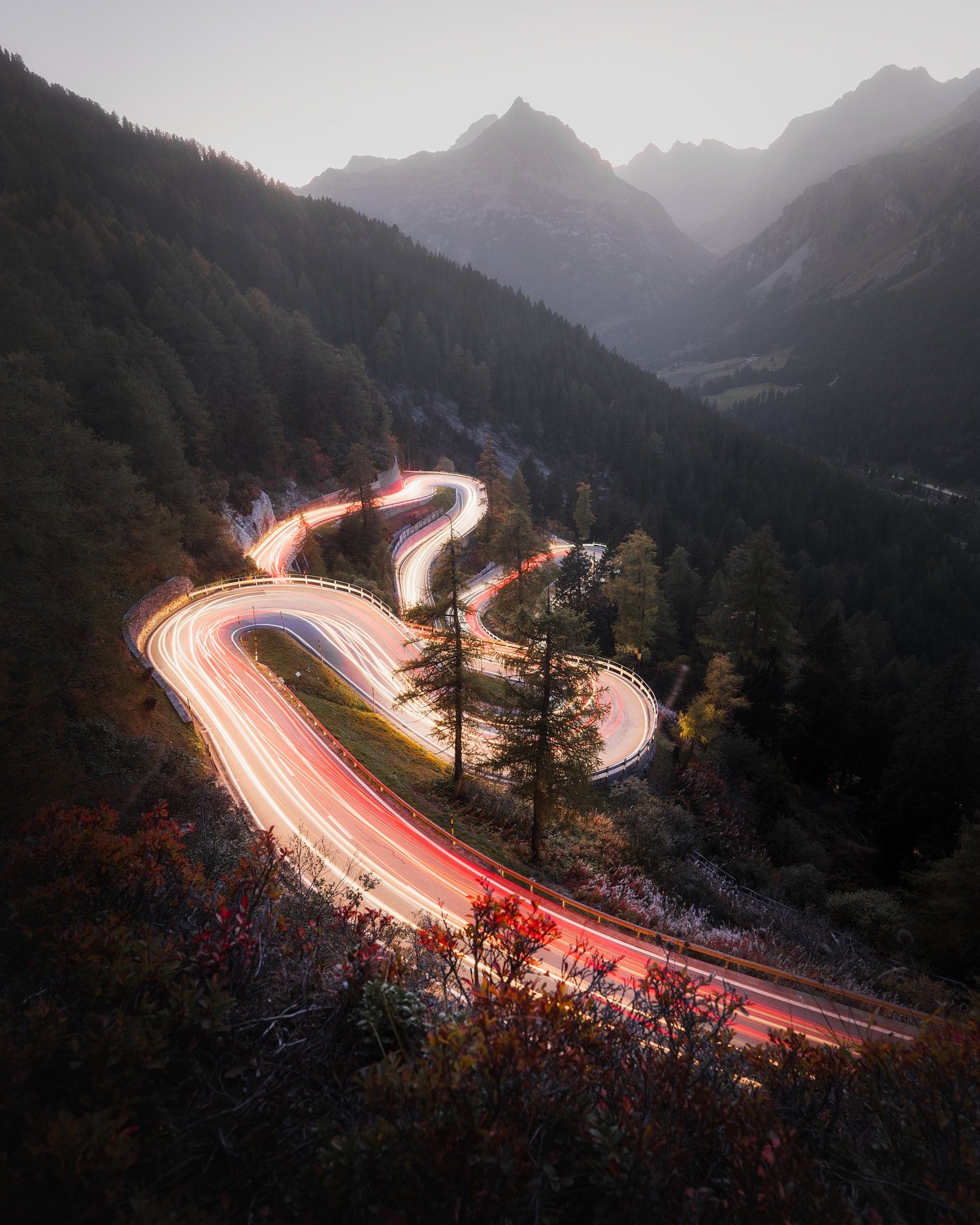 Eine kurvige Strasse am Malojapass zieht sich durch die Berge im warmen Abendlicht.